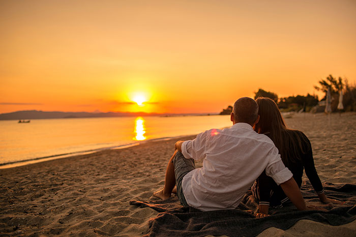 couple sitting on beach watching sunset over ocean