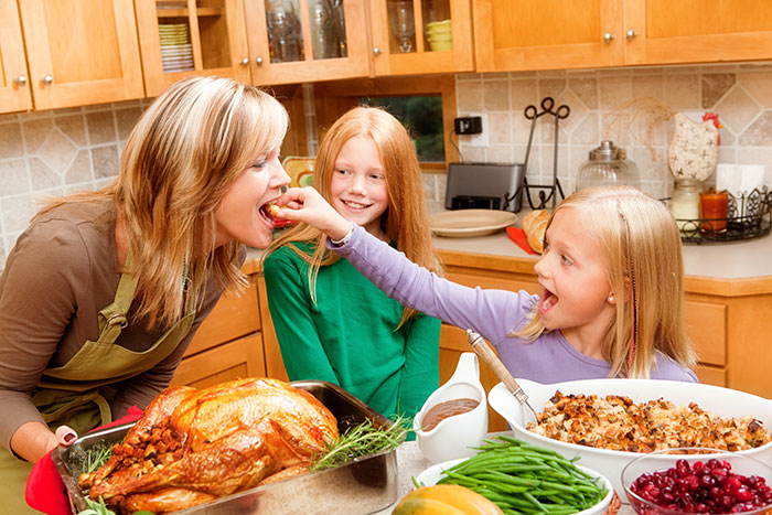 mother and two daughters with thanksgiving feast in kitchen with roasted turkey, green beans, stuffing, and cranberries