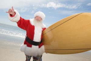 Happy senior Santa Claus gesturing with surf board on beach