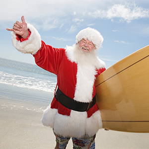 Happy senior Santa Claus gesturing with surf board on beach